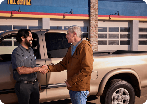 Mechanic and customer shaking hands in front of a beige pickup truck outside an automotive service center.
